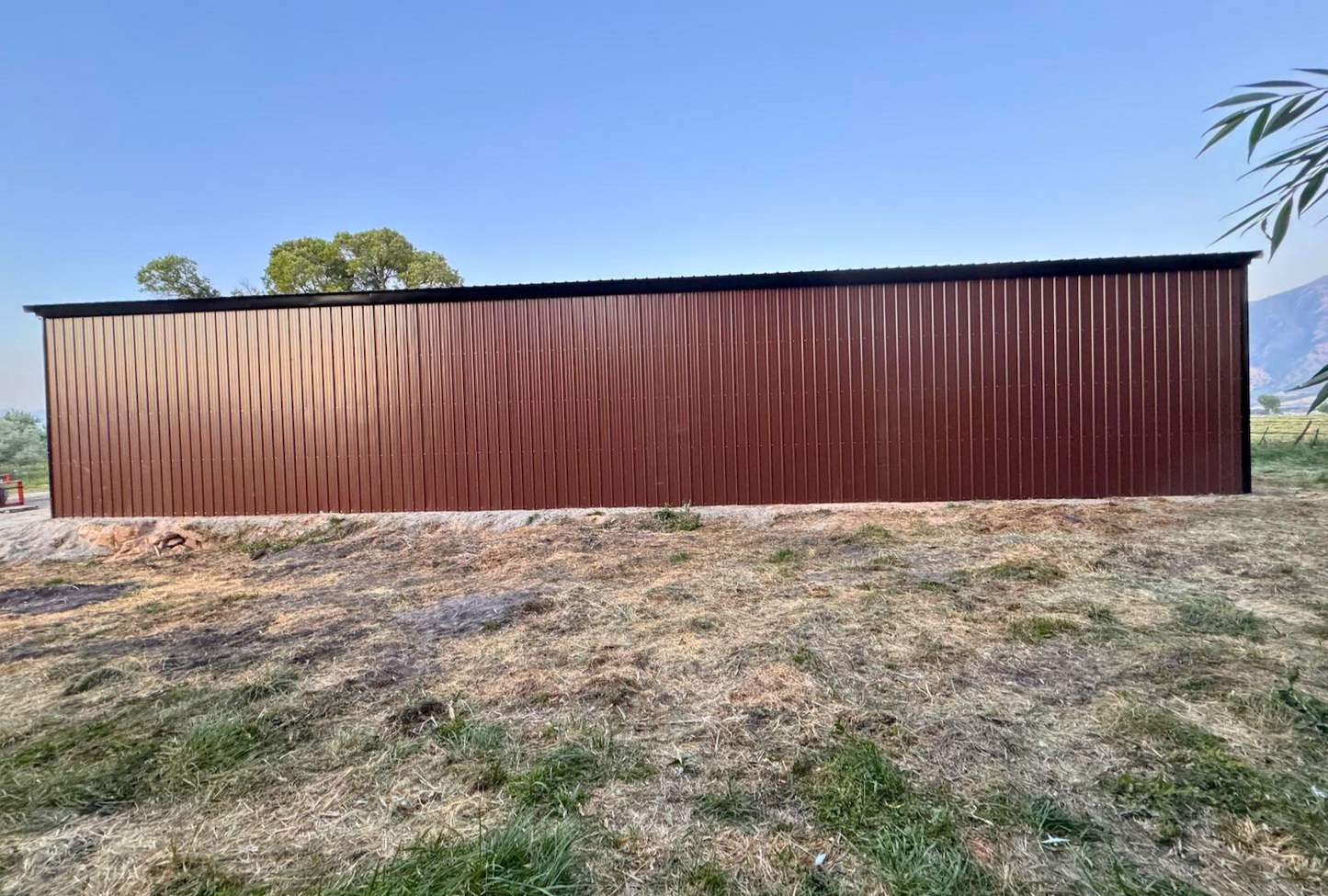 Outside right view of 36'x80'x14' steel hay shop features ladder style truss design, vertical roof, 14 Ga. frame, 40PSF ground snow load, both sides, back end & front gable end enclosed with vertical siding, lateral & back end diagonal bracing.