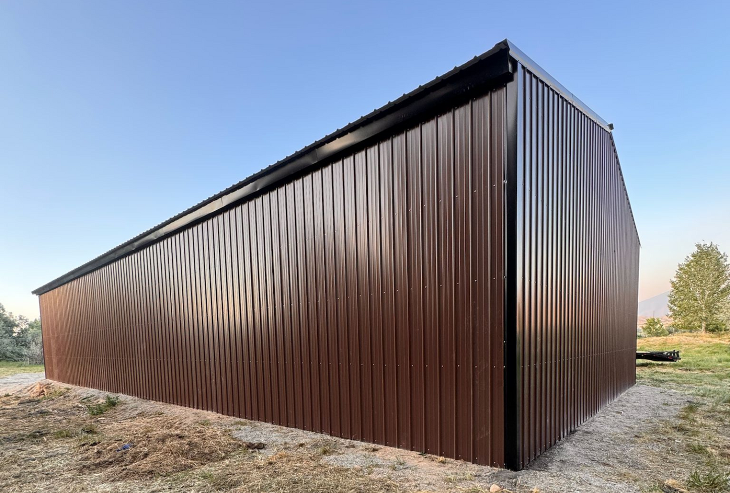 Outside back right view of 36'x80'x14' steel hay shop features ladder style truss design, vertical roof, 14 Ga. frame, 40PSF ground snow load, both sides, back end & front gable end enclosed with vertical siding, lateral & back end diagonal bracing.