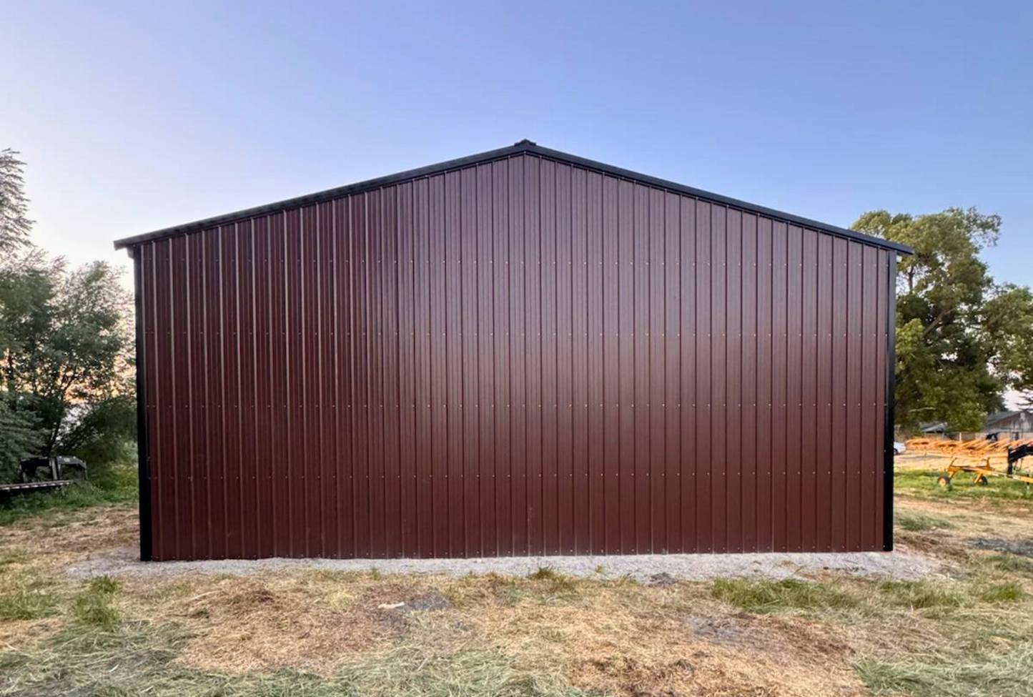 Outside back view of 36'x80'x14' steel hay shop features ladder style truss design, vertical roof, 14 Ga. frame, 40PSF ground snow load, both sides, back end & front gable end enclosed with vertical siding, lateral & back end diagonal bracing.