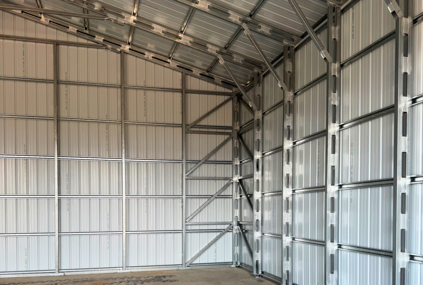 Inside right view of 40'x40'x15' steel shop features ladder style truss design, vertical roof, 14 Ga. frame, 30PSF ground snow load, fully enclosed with vertical siding, one 36" x 80" walk-in door, and two 12' x 14' overhead door frame outs on the end.