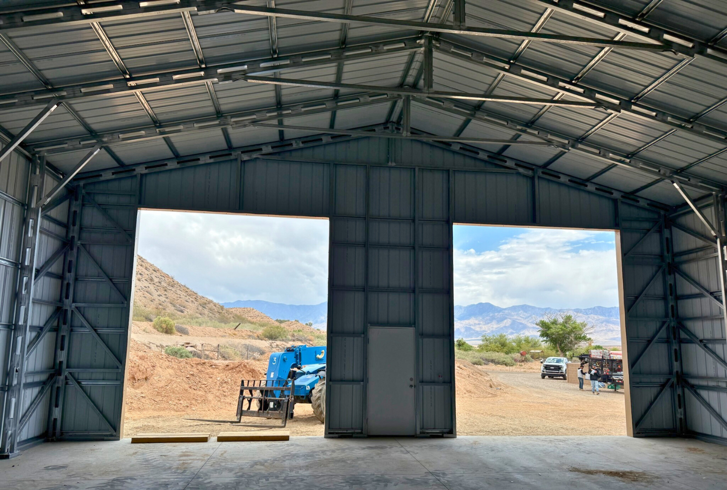 Inside front view of 40'x40'x15' steel shop features ladder style truss design, vertical roof, 14 Ga. frame, 30PSF ground snow load, fully enclosed with vertical siding, one 36" x 80" walk-in door, and two 12' x 14' overhead door frame outs on the end.