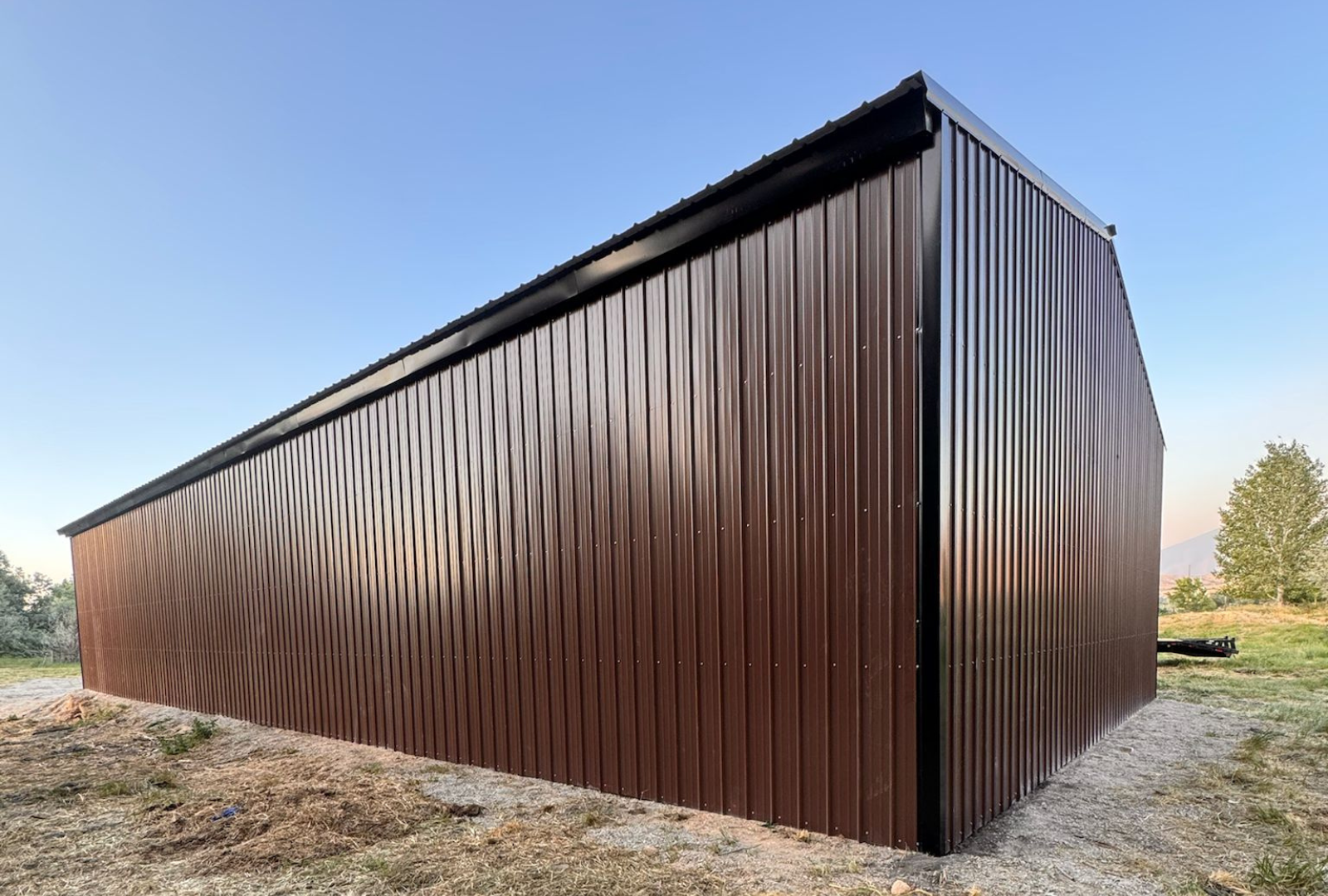 Outside back right view of 36'x80'x14' steel hay shop features ladder style truss design, vertical roof, 14 Ga. frame, 40PSF ground snow load, both sides, back end & front gable end enclosed with vertical siding, lateral & back end diagonal bracing.