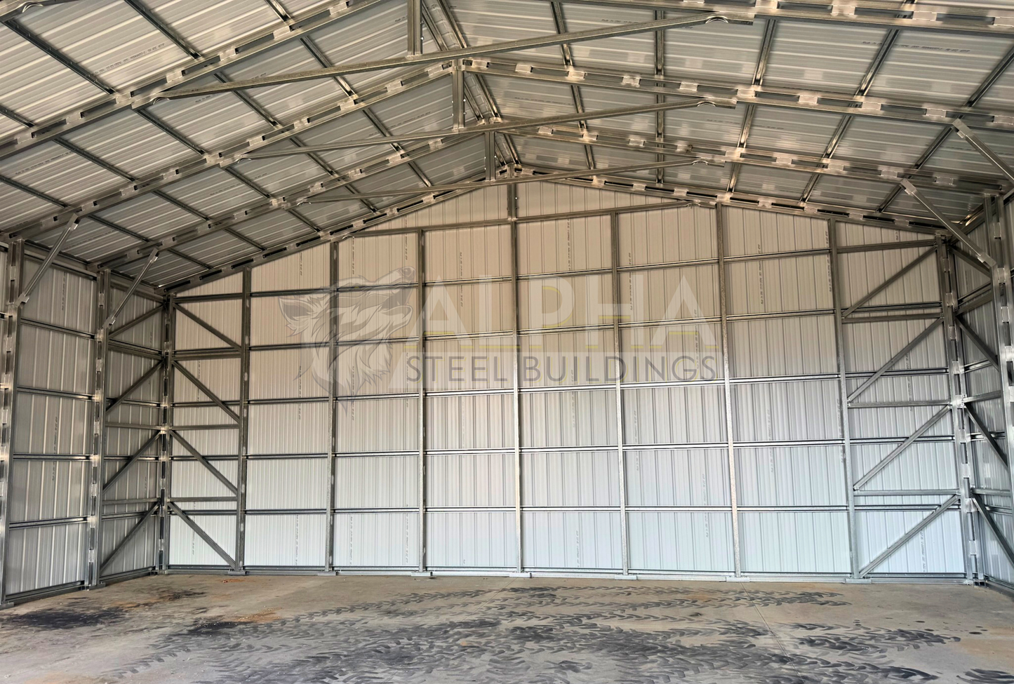 Internal back view of 40'x40'x15' steel shop features ladder style truss design, vertical roof, fully enclosed with vertical siding, one 36" x 80" walk-in door, and two 12' x 14' overhead door frame outs on the end. 