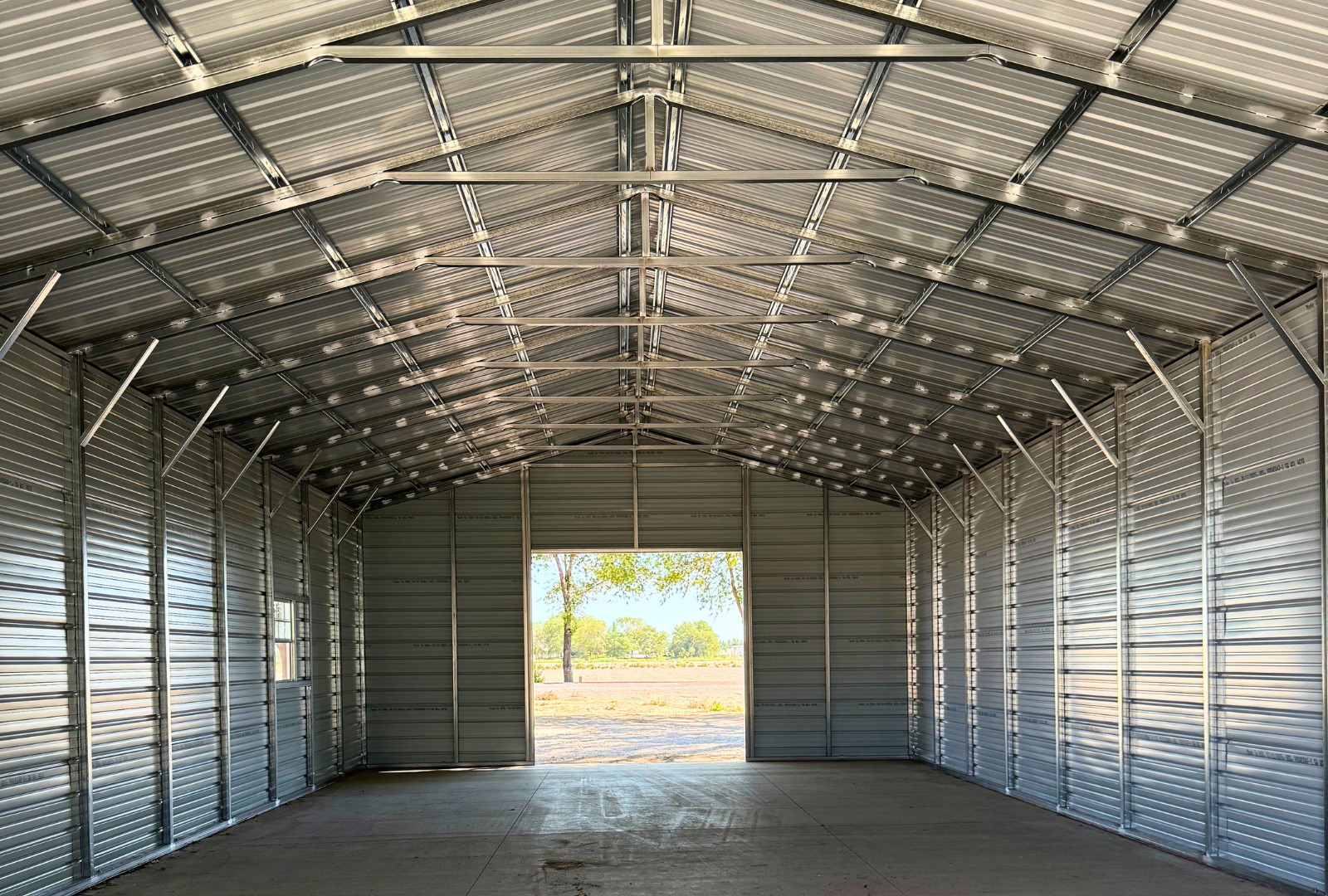 26x60x12 A-frame steel building with vertical roof, (1) 12' x 12' overhead door frame out on the end, (1) 10' x 10' overhead door frame out on the end, (1) 36" x 80" walk-in door on the side, (2) 30" x 36" windows on the side, inside view.
