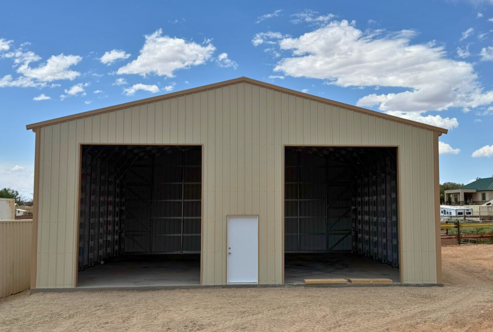 Outside front view of 40'x40'x15' steel shop features ladder style truss design, vertical roof, 14 Ga. frame, 30PSF ground snow load, fully enclosed with vertical siding, one 36" x 80" walk-in door, and two 12' x 14' overhead door frame outs on the end. 