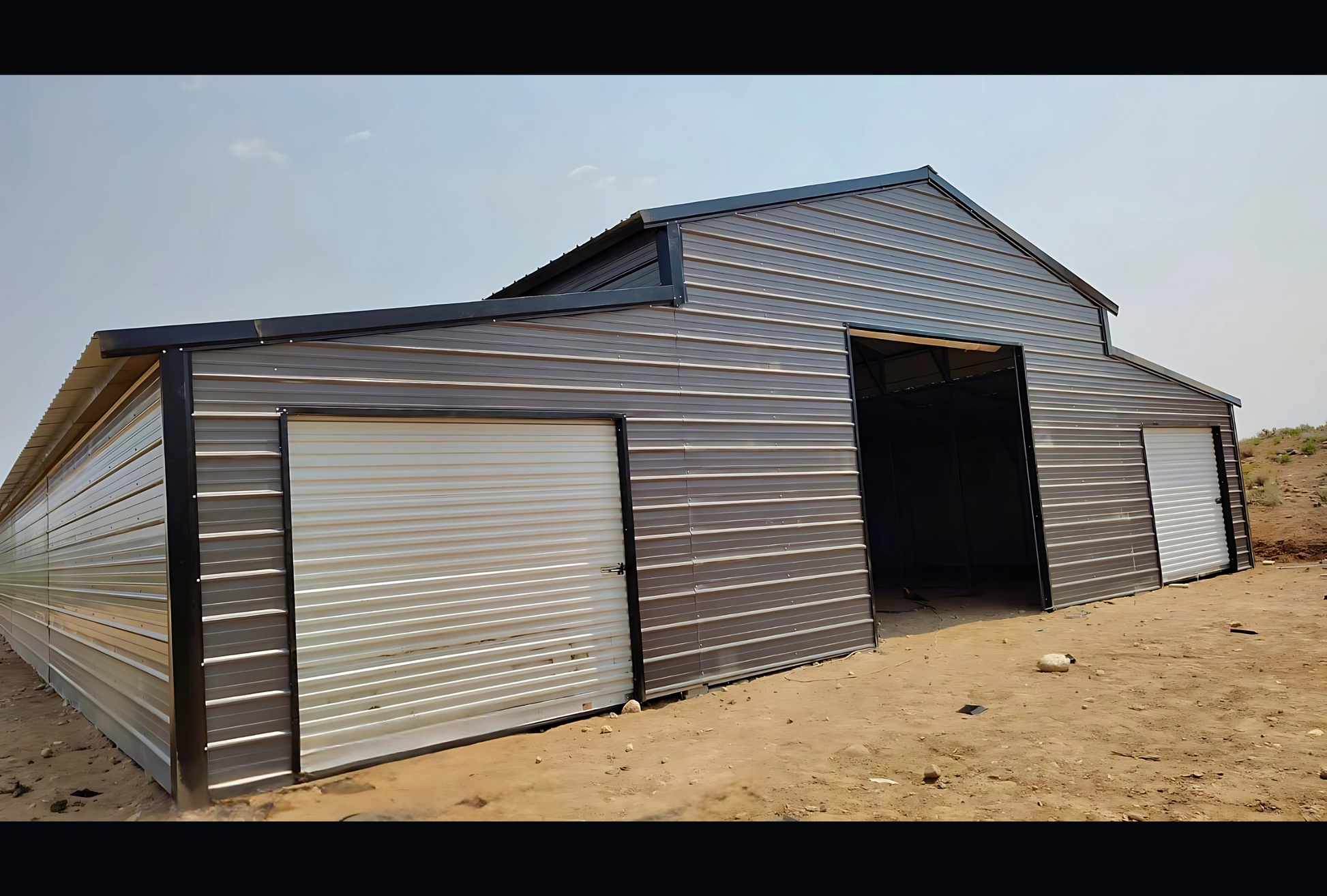 Front left view of 48' x 100' steel barn with lean-tos, and garage doors for livestock or farm equipment storage.